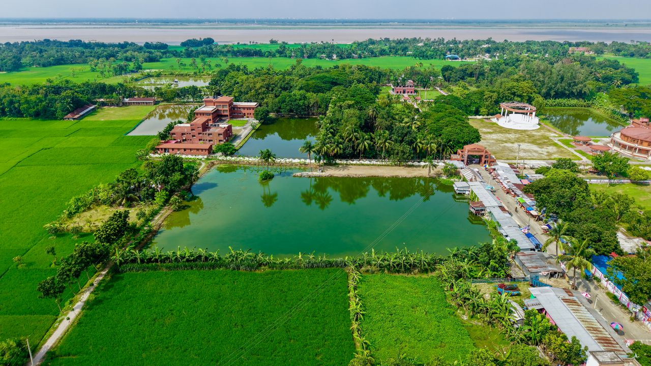 Aerial photo of a lush Indian village surrounded by rice fields, ponds, and greenery.